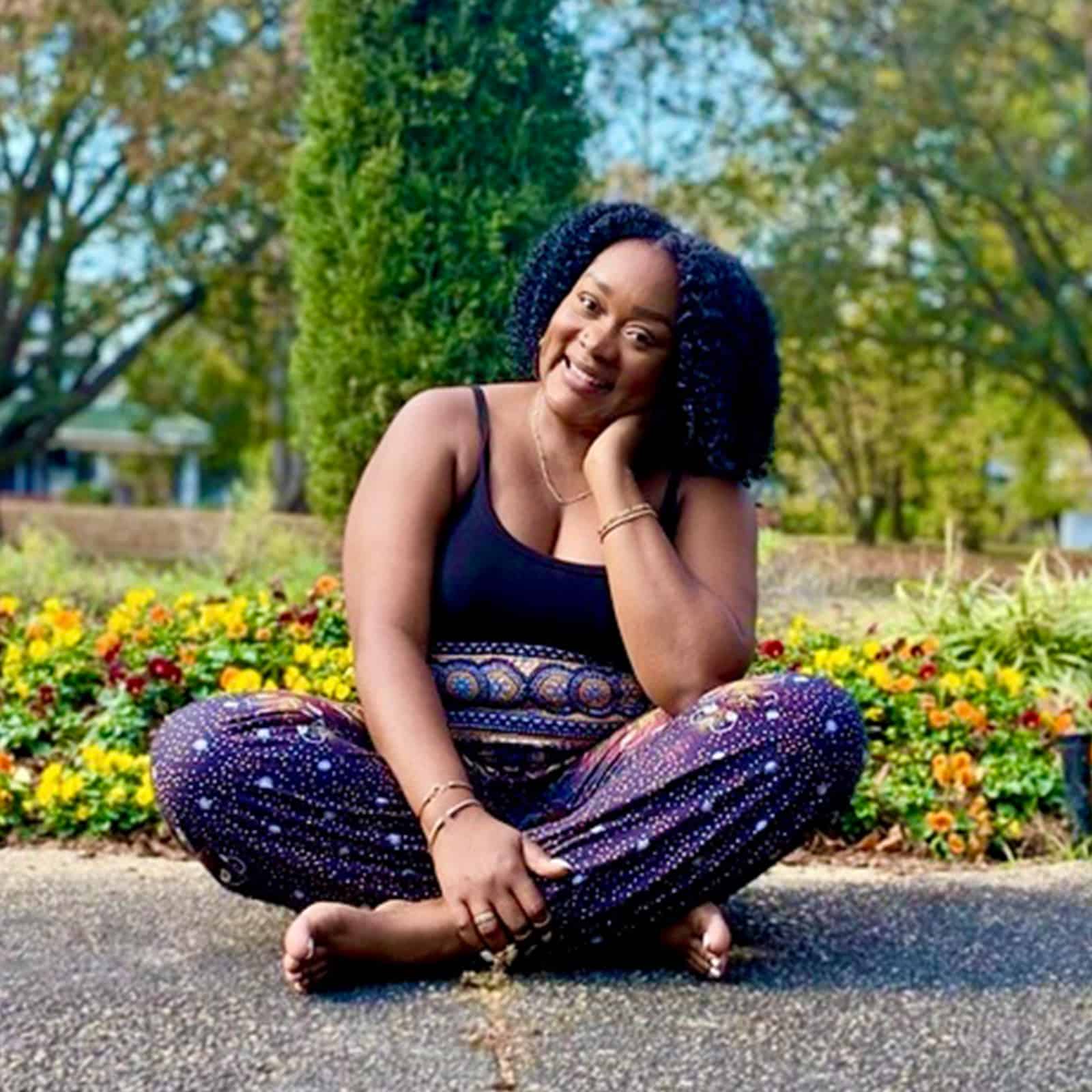 Victoria T. Traylor sitting cross-legged in a garden, smiling
